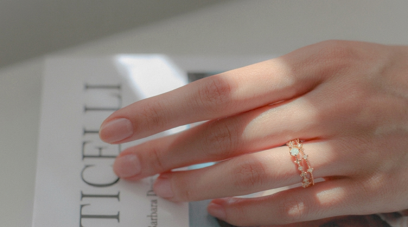 Alt Text: A close-up photograph of a person's hand resting on an open magazine page, wearing delicate gold rings on the ring finger, with soft natural light and a cinematic moody atmosphere.